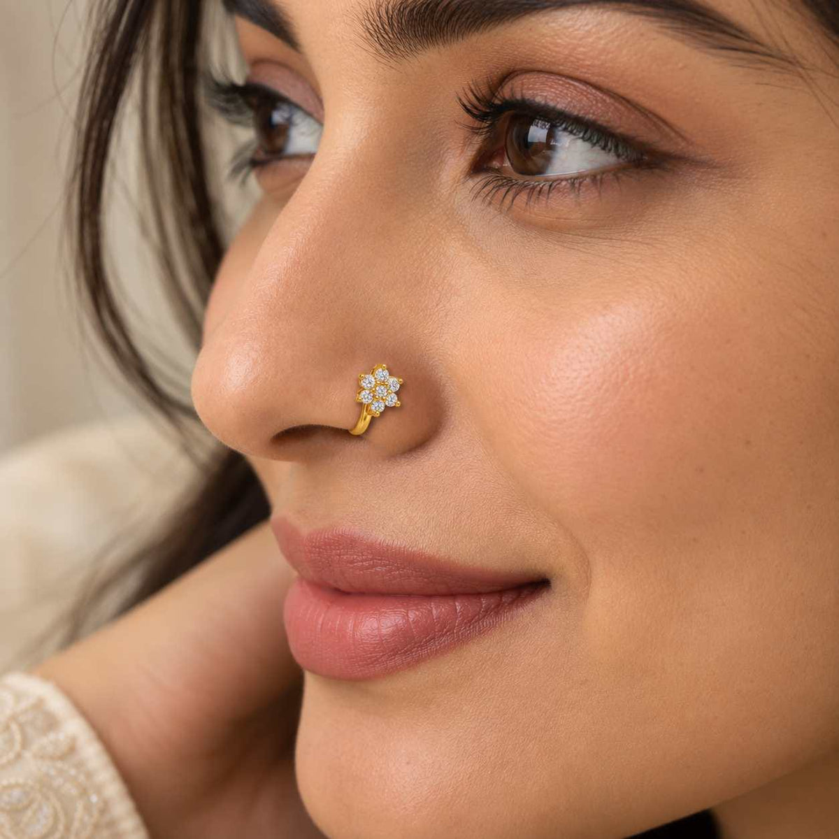 A close-up of a woman's face wearing a small gold nose stud with clear stones on her left nostril.