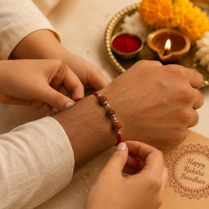 A close-up lifestyle shot of a person's wrist being adorned with a traditional Indian Rakhi bracelet. The bracelet features red thread , rudrkasha and 925 silver, with hands adjusting it.