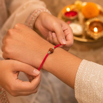 A close-up of sister tieing 925 silver rudraksha rakhi on brother's wrist on raksha bandhan. 