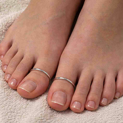 Close-up of feet with silver thumb plain toe rings on a textured surface